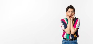 Şok olmuş genç adam çene aşağı, kameraya bakarak etkilenmiş ve nutku tutulmuş, beyaz arka plan üzerinde duran.