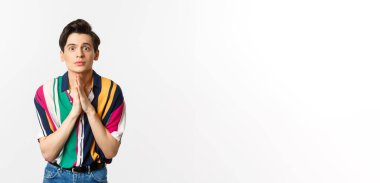 Yardım için yalvaran, kameraya bakıp yardım dilenen, tavsiye isteyen, beyaz arka planda duran umut dolu genç bir adam..