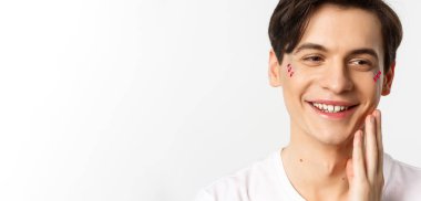Millet, lgbtq ve güzellik konsepti. Yüzünde parıltı olan, gülümseyen ve mutlu görünen, yanaktan yanağa dokunan, beyaz arka planda güzel bir gay adamın vesikalığı..