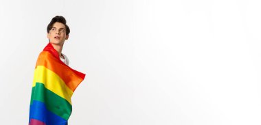 İnsan hakları ve lgbtq toplum kavramı. Yüzünde parıltı olan, gökkuşağı gurur bayrağı takan ve sol üst köşede beyaz arka planda güzel, çift cinsiyetli genç bir adam..