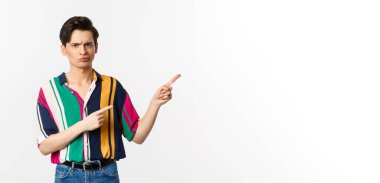 Şüpheci ve hoşnutsuz genç bir adam endişeli, parmakları düzgün ve onaylanmamış, beyaz arka planda duran.