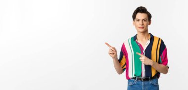 Tarz sahibi çift cinsiyetli bir adamın gülümsemesi, logoyu işaret etmesi, reklam teklifini göstermesi, beyaz arka planda durması..