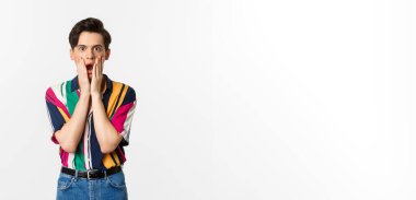 Yakışıklı çift cinsiyetli adamın portresi. Şok olmuş, nefes nefese kalmış, el ele tutuşmuş, hayret içinde kameraya bakıyor, beyaz arka planda dikiliyor..