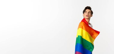 İnsan hakları ve lgbtq toplum kavramı. Yüzünde parıltı olan, gökkuşağı gurur bayrağı takan ve sol üst köşede beyaz arka planda güzel, çift cinsiyetli genç bir adam..