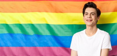 Yüzünde sim olan, mutlu ve gururlu gülümseyen, gökkuşağı gurur bayrağına, lgbtq topluluk haklarına ve insanların kavramına karşı duran güzel eşcinsel adam..