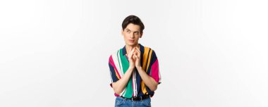 Sinsi genç adamın bir planı var. Çan kulesi gibi parmakları var ve sol üst köşede kurnaz görünüyor. Bir şeyler planlıyor, beyaz arka planda duruyor..