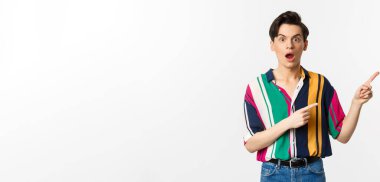 Etkilenmiş genç bir adam reklamını yapıyor, ağzı kulaklarıyla açık ve sağ üst köşeyi işaret ediyor, beyaz arka planda duruyor..