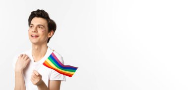 Yüzünde parıltı olan çekici bir gay adamın belden yukarısında sallanan gökkuşağı bayrağı ve sol üst köşede rüya gibi görünen lgbtq konsepti..