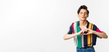 Güzel genç adam dudaklarını büzüyor ve kalp işareti gösteriyor. Öpüşmeyi bekliyor. Seni seviyorum..