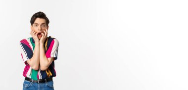 Şok olmuş genç adam çene aşağı, kameraya bakarak etkilenmiş ve nutku tutulmuş, beyaz arka plan üzerinde duran.