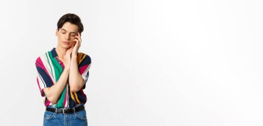 Genç çekici adam nazikçe yüzüne dokunuyor, gözlerini kapatıyor ve hayal kuruyor, beyaz arka planda duruyor..