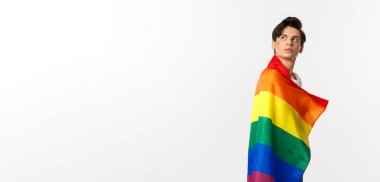 lgbtq bayrağı takan düşünceli genç bir gay resmi, başınızı sol üst köşeden çevirin, logoya bakın, beyaz arka planda dikilen.