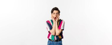 Şok olmuş genç adam çene aşağı, kameraya bakarak etkilenmiş ve nutku tutulmuş, beyaz arka plan üzerinde duran.