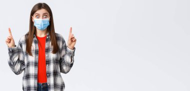 Coronavirus salgını, karantina, sosyal mesafeler ve duygu kavramı. Şaşkınlık ve şaşkınlık içinde, tıbbi maskeli çekici bir kadın, tanıtım ya da bağlantı gösteriyor, parmaklarını havaya kaldırıyor..