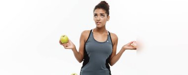 Sağlıklı ve diyet kavramı - güzel sportif Afrikalı-Amerikalı çörek ve yeşil elma arasında bir karar olun. Beyaz arka plan üzerinde izole