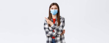 Coronavirus salgını, karantina, sosyal mesafeler ve duygu kavramı. Tıbbi maskeli neşeli beyaz kadın, sol üst köşeyi işaret ediyor, link ya da ürün öneriyor..
