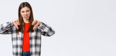 Yaşam tarzı, farklı duygular, boş zaman aktiviteleri konsepti. Hoşnutsuz ve etkilenmemiş, seçici kız işaretli gömlek, baş parmak aşağı ve beğenmediklerini ifade etmek için dilini göster, berbat film derecesi.