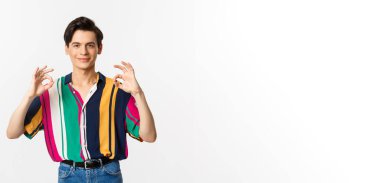 Tatmin olmuş, genç, eşcinsel bir adam onay veriyor ve gülümsüyor. Katılıyorum ve bir şey gibi, mükemmel bir seçim, beyaz arka planda duruyor..