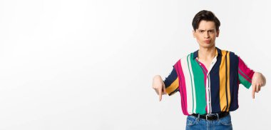 Şüpheci ve hoşnutsuz ibne adam parmaklarını eğip, kötü bir şeyi eleştiriyor ve beyaz arka planda duruyor..