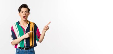 Etkilenmiş genç bir adam reklamını yapıyor, ağzı kulaklarıyla açık ve sağ üst köşeyi işaret ediyor, beyaz arka planda duruyor..