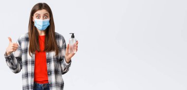 Coronavirus salgını, karantina, sosyal mesafeler ve duygu kavramı. Şaşırmış ve etkilenmiş tıbbi maskeli bir kız, virüse yakalanmasını engellemek istiyor, el dezenfektanı kullanıyor..