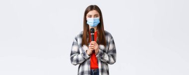 Coronavirus salgını, karantina, sosyal mesafeler ve duygu kavramı. Tıbbi maskeli kız şarkı söylüyor ya da stand-up yapıyor, mikrofon tutuyor, duyulmak istiyor, beyaz arkaplan.