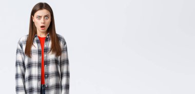 Yaşam tarzı, farklı duygular, boş zaman aktiviteleri konsepti. Şok olmuş ve kafası karışmış çekici bir kız öğrenci garip, şaşırtıcı bir haber duyar, çenesini indirir ve şaşkın bir şekilde kameraya bakar.