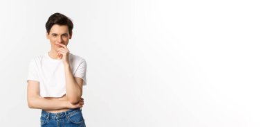 Lgbtq ve gurur konsepti. Tatmin olmuş genç eşcinsel bir adam, bir fikre sahip olmak ve kameraya bakarken gülümsemek, ekşi bluz, beyaz arka plan.