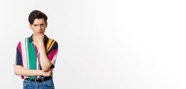 Hüzünlü gay adamın görüntüsü, kameraya bakıyor, somurtuyor ve üzgün, el üstünde duruyor, beyaz arka planda duruyor..