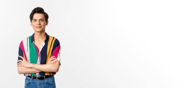 Güzel görünümlü genç adam göğsünde çapraz kollar, kameraya gülümsüyor, beyaz arka planda duruyor..