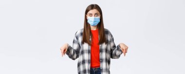 Coronavirus salgını, karantina, sosyal mesafeler ve duygu kavramı. Şok olmuş ve etkilenmiş tıbbi maskeli ve günlük kıyafetli genç bir kadın, parmakla işaret ediyor, kameraya bakıyor..