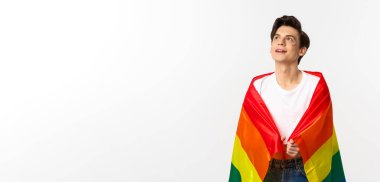 İnsan hakları ve lgbtq toplum kavramı. Yüzünde parıltı olan, gökkuşağı gurur bayrağı takan ve sol üst köşede beyaz arka planda güzel, çift cinsiyetli genç bir adam..