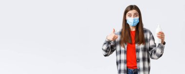 Coronavirus salgını, karantina, sosyal mesafeler ve duygu kavramı. Tıbbi maskeli heyecanlı ve tatmin olmuş bir kız el dezenfektanı, virüs sabununu ve parmak uçlarını önlüyor..