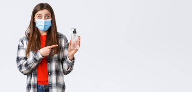 Coronavirus salgını, karantina, sosyal mesafeler ve duygu kavramı. Tıbbi maskeli, el dezenfektanını işaret eden heyecanlı ve şaşkın genç kadın,.