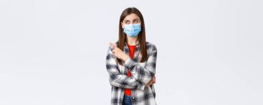 Coronavirus salgını, karantina, sosyal mesafeler ve duygu kavramı. Tıbbi maskeli genç kız evde kalıyor, iş arıyor, sol üst köşeyi işaret ediyor..