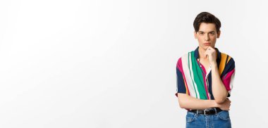 Yakışıklı ve şık bir adamın portresi kameraya düşünceli bakıyor, seçim yapıyor, sana bakmayı düşünüyor, beyaz arka planda duruyor..