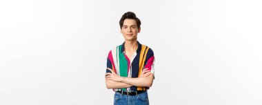 Güzel görünümlü genç adam göğsünde çapraz kollar, kameraya gülümsüyor, beyaz arka planda duruyor..