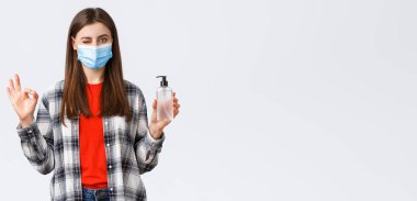 Coronavirus salgını, karantina, sosyal mesafeler ve duygu kavramı. Hiç sorun değil. Tıbbi maskeli hoş kız el dezenfektanı gibi işaret ve göz kırp..
