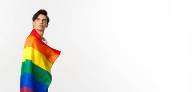 lgbtq bayrağı takan düşünceli genç bir gay resmi, başınızı sol üst köşeden çevirin, logoya bakın, beyaz arka planda dikilen.