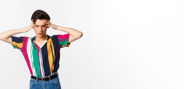 Arsız çift cinsiyetli adam kameraya bakıyor, delici bakışlarla sana bakıyor, beyaz arka planda duruyor..