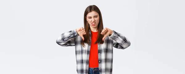 生活方式 不同的情感 休闲活动的概念 穿着格子衬衫 垂下大拇指 露出舌头表示不喜欢的年轻挑剔姑娘 对糟糕的电影进行评分 — 图库照片