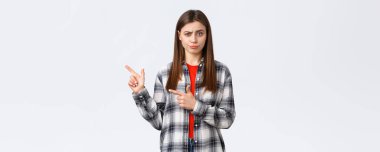 Yaşam tarzı, farklı duygular, boş zaman aktiviteleri konsepti. Şüpheci ve etkilenmemiş kızın şüpheci düşünceleri, şüpheciliği ve şüpheciliği ifade eder, parmaklarını sola uzatır ve hoşnutsuzca sırıtır..