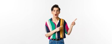 Etkilenmiş genç bir adam reklamını yapıyor, ağzı kulaklarıyla açık ve sağ üst köşeyi işaret ediyor, beyaz arka planda duruyor..