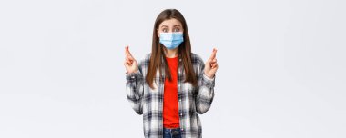 Coronavirus salgını, karantina, sosyal mesafeler ve duygu kavramı. Umut dolu iyimser maskeli tatlı kız inançlı, şans diliyor ya da dua ediyor..
