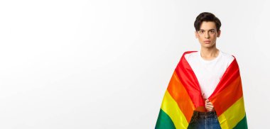 Ciddi görünümlü cinsiyet değişkeni yüzü simli, lgbtq gökkuşağı bayrağı takan, beyaz arka planda duran biri..