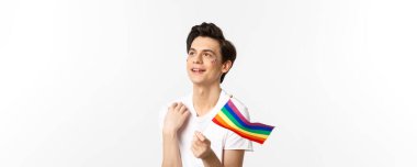 Yüzünde parıltı olan çekici bir gay adamın belden yukarısında sallanan gökkuşağı bayrağı ve sol üst köşede rüya gibi görünen lgbtq konsepti..