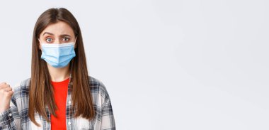 Coronavirus salgını, karantina, sosyal mesafeler ve duygu kavramı. Şüpheci, etkilenmemiş, tıbbi maskeli güzel bir kadın baş parmağını sola uzatıyor ve kaşlarını çatıyor..