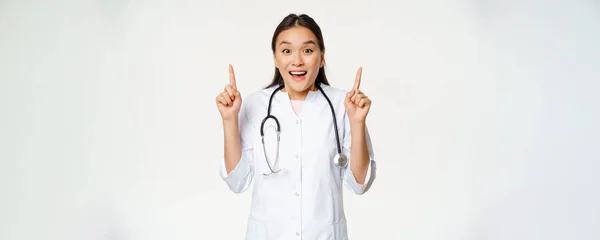 興奮した笑顔の看護師 医師の制服を指摘し プロモーション販売 医療クリニック割引を示し 白い背景の上に立って — ストック写真