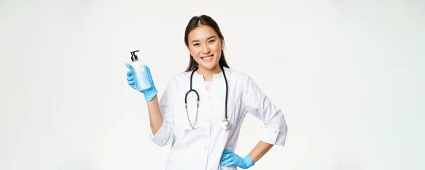 Usmívající Asijský Lékař Drží Ruční Dezinfekci Gumových Rukavicích Ukazuje Láhev — Stock fotografie