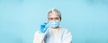 Asyalı kadın doktor portresi yakın çekim, kişisel koruyucu ekipman hemşiresi aşıyı gösteren şırınga, grip aşısı ya da mavi arka plan.